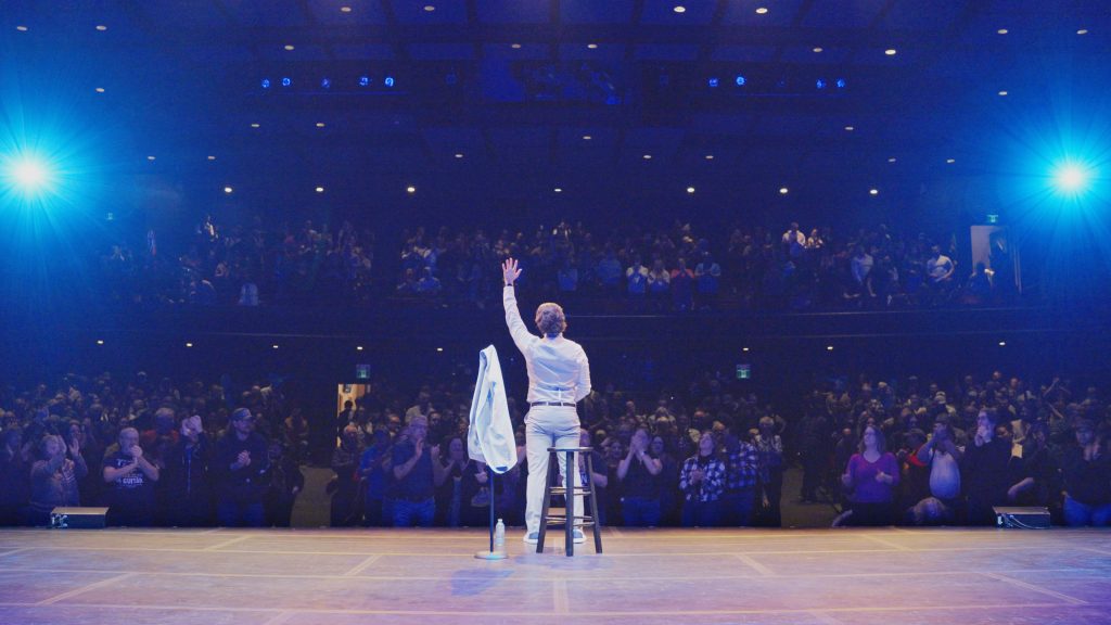 Alex Mackenzie on stage in front of a standing audience